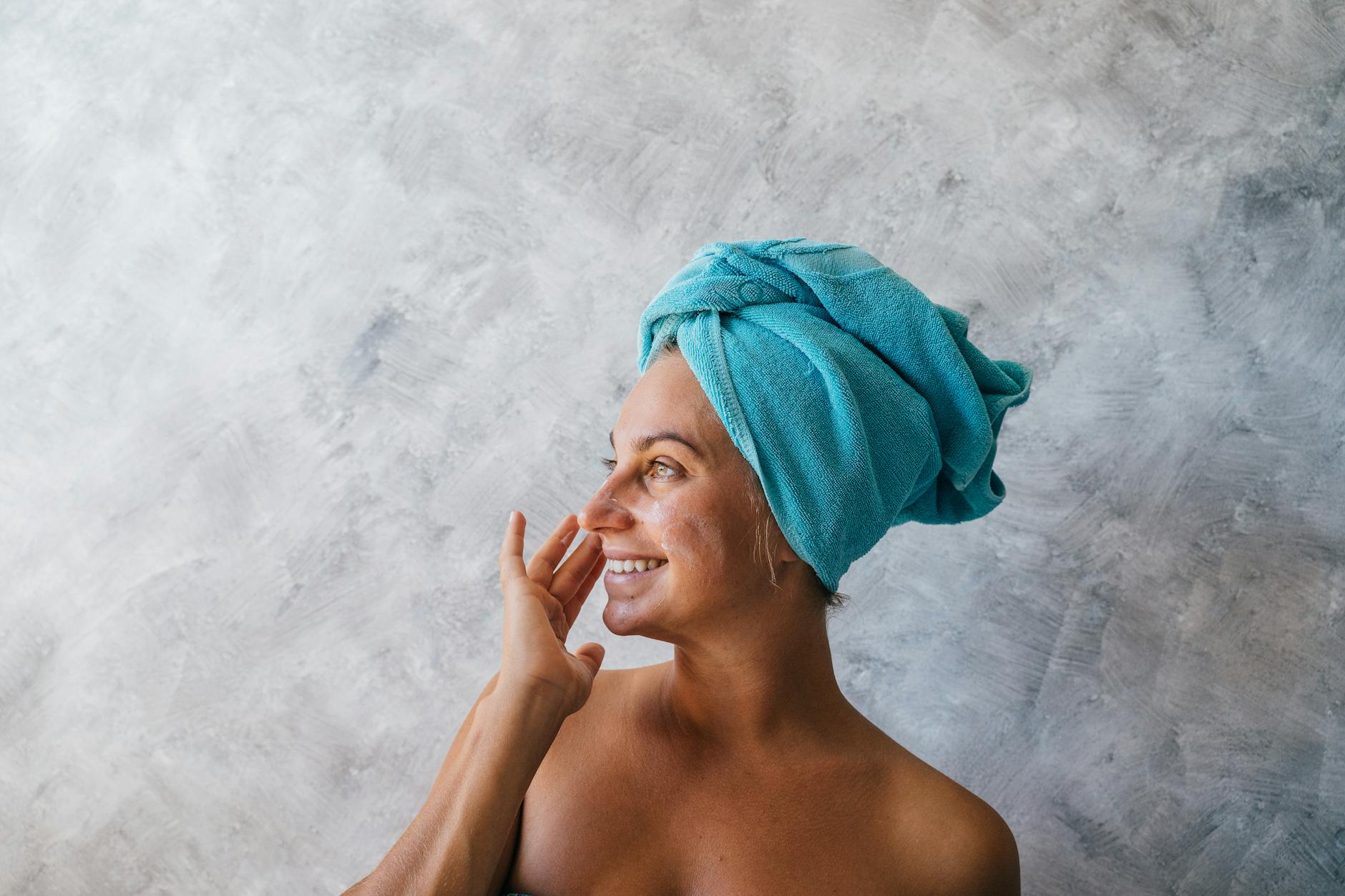 a woman with towel on head applying facial cream